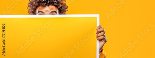 person peeking from behind a blank canvas, with only their eyes and forehead visible, set against a monochromatic orange background, expressing curiosity or surprise. photo