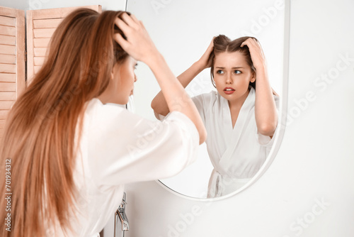 Worried young woman with hair loss problem looking in mirror at home