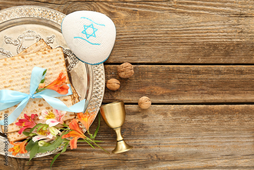 Passover Seder plate with flatbread matza, kippah, wine cup, walnuts and alstroemeria flowers on wooden background