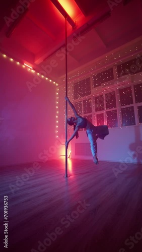 Elegant Woman Performs a Pole Dance Under Neon Lighting. Aerial Gymnastics. Modern Sports and Athleticism Concept. Healthy Lifestyle and Female Beauty. Slow Motion. Vertical Video. photo