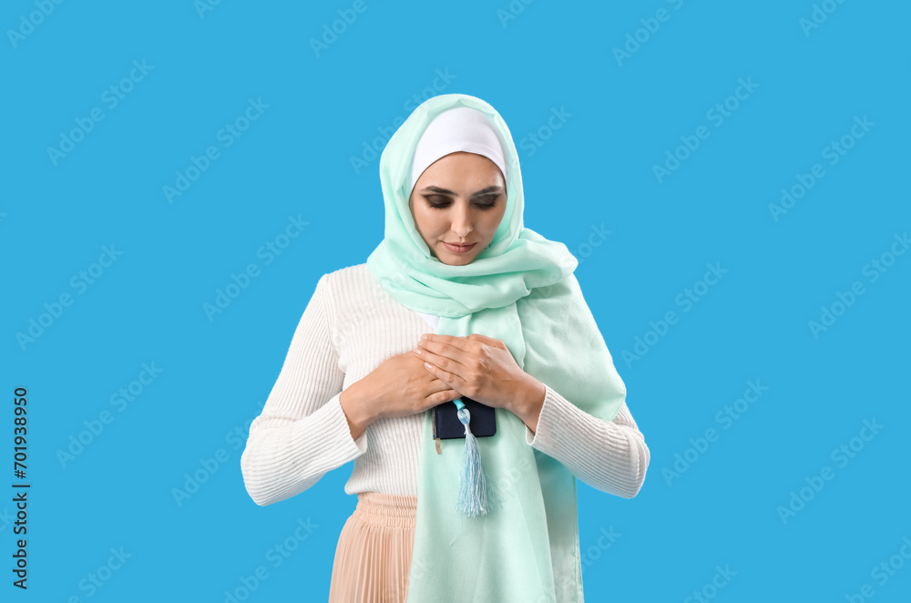 Young Muslim woman with Koran and prayer beads on blue background. Islamic New Year celebration Young Muslim woman with Koran and prayer beads on blue background. Islamic New Year celebration