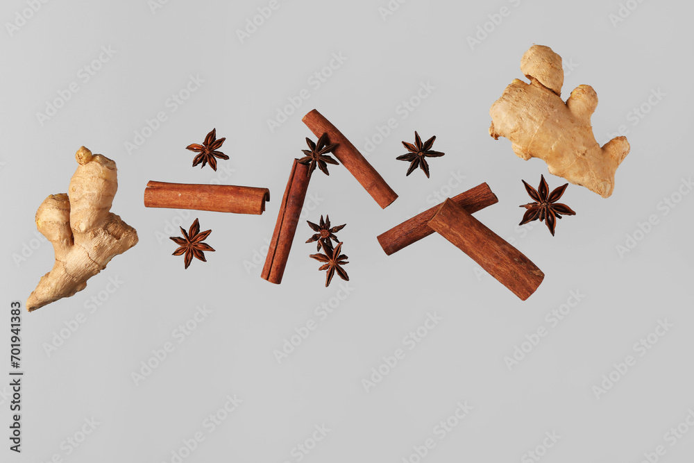Flying cinnamon sticks, anise stars and ginger roots on grey background - obrazy, fototapety, plakaty 