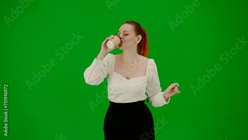 Portrait of attractive office girl on chroma key green screen. Woman in skirt and blouse holding paper cup drinking coffee and dancing cutely.
