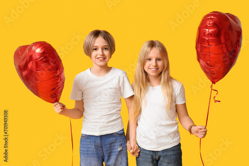 Little children with heart-shaped balloons holding hands on yellow background. Valentine's Day celebration