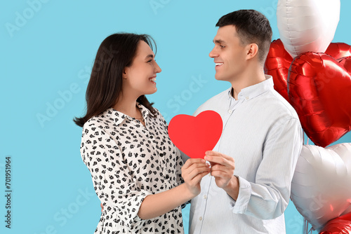 Young couple with paper heart and balloons on blue background. Valentine's Day celebration