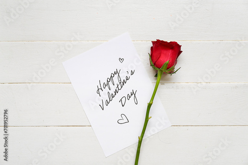Card with text HAPPY VALENTINE'S DAY and red rose on white wooden background