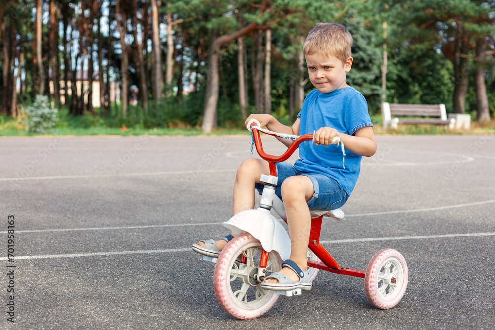 A cute very satisfied child is driving his old tricycle in the city outdoor basketball court A cute very satisfied child is driving his old tricycle in the city outdoor basketball court