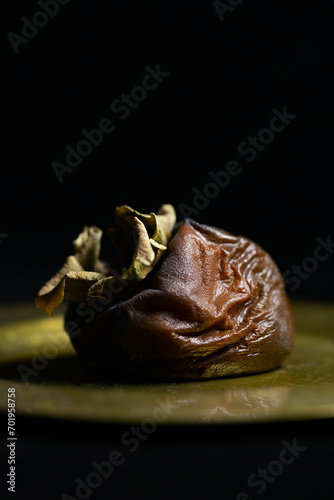 A dark, wrinkled and rotting persimmon fruit against a black background.
