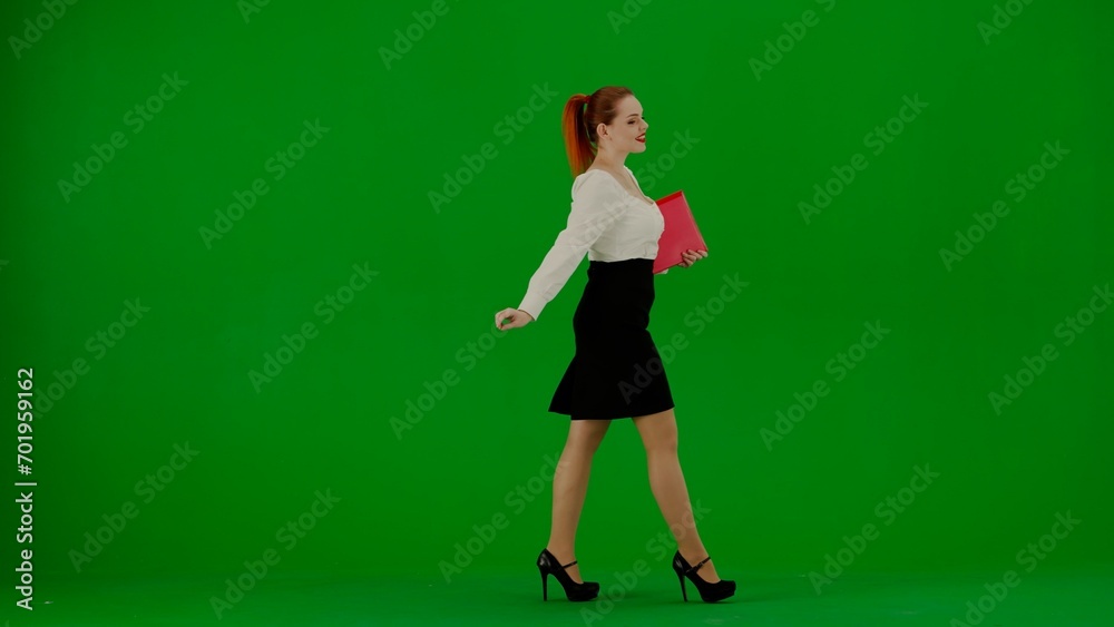 Portrait of attractive office girl on chroma key green screen. Woman in skirt and blouse walking cutely with red paper folder, smiling expression.