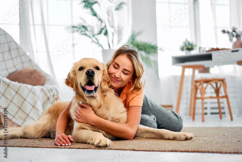Love to pet. Adorable woman with closed eyes embracing adult golden retriever while lying together on floor. photo