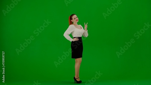 Portrait of attractive office girl on chroma key green screen. Woman in skirt and blouse standing smiling at camera showing victory sign. © kinomaster