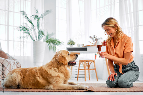 Animal companion. Caucasian woman sitting on floor next to well behaved fluffy dog and showing new toy. Affectionate female keeper giving canine friend sincere love and attention at living room. photo