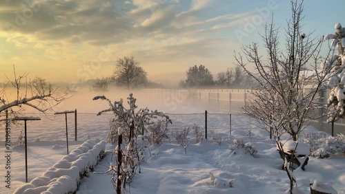 Moving fog with orange sunlight during sunrise over fields with snow behind garden with fence near noise barriers along national road in Poland with horizon with trees - timelapse. photo