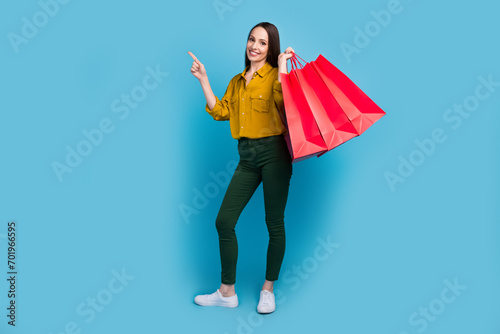 Full length photo of excited cheerful lady wear yellow shirt rising bargains pointing empty space isolated blue color background