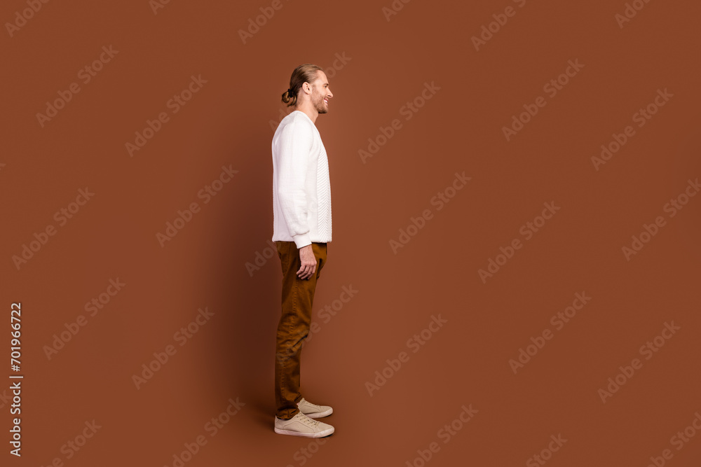 Full length photo of handsome positive man wear white sweater looking empty space isolated brown color background