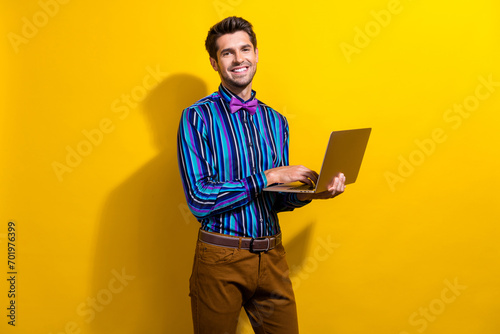 Photo of intelligent clever man dressed striped shirt bow tie typing email on laptop at work isolated on vivid yellow color background