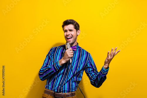 Photo of handsome man dressed striped shirt bow tie sing pop song in microphone on scene at party isolated on yellow color background photo