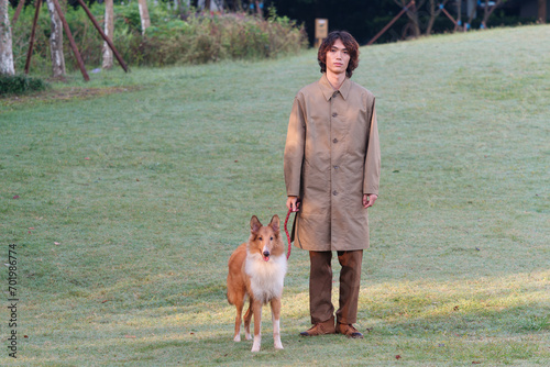Photos Portrait of a handsome Chinese young man in khaki overcoat with his rough collie dog on green grass field in sunny day, male fashion, cool Asian young man lifestyle, harmony man and pet