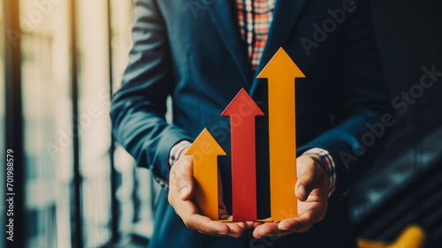 
A businessman holding upward arrows symbolizing a business project management strategy. The focus is on controlling costs, improving product quality, and enhancing service concepts.