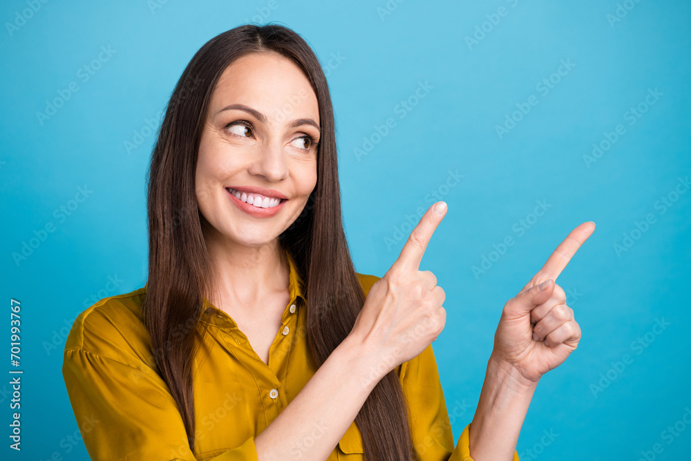 Photo of dreamy positive lady wear yellow shirt looking pointing two fingers empty space isolated blue color background Photo of dreamy positive lady wear yellow shirt looking pointing two fingers empty space isolated blue color background