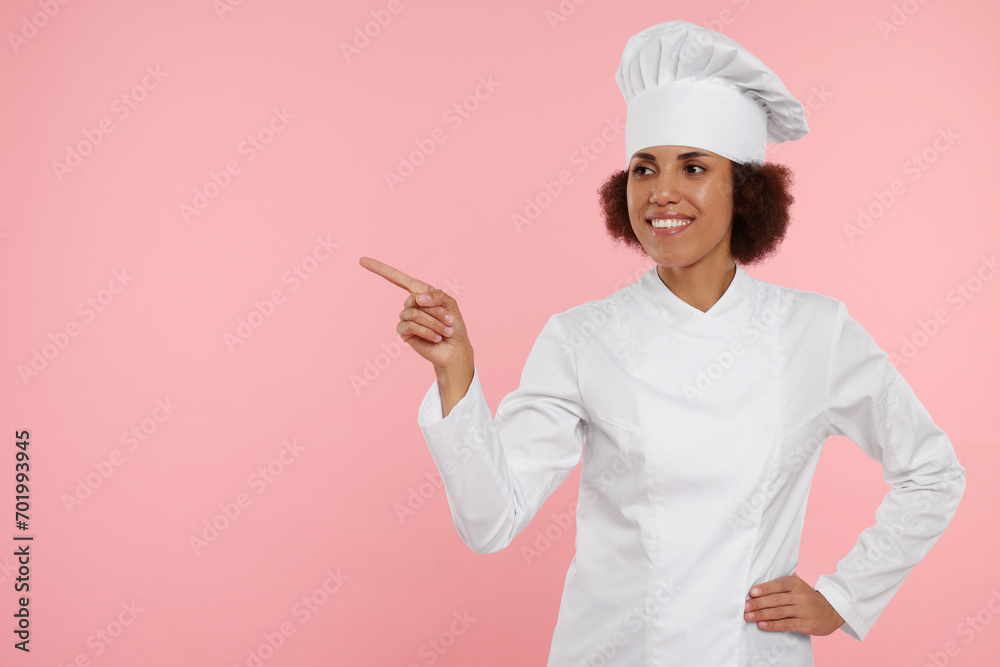 Happy female chef in uniform pointing at something on pink background. Space for text Happy female chef in uniform pointing at something on pink background. Space for text