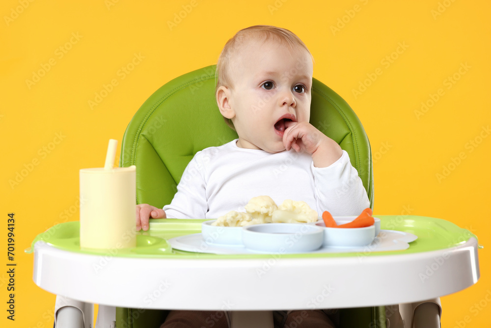 Cute little baby with healthy food in high chair on orange background Cute little baby with healthy food in high chair on orange background