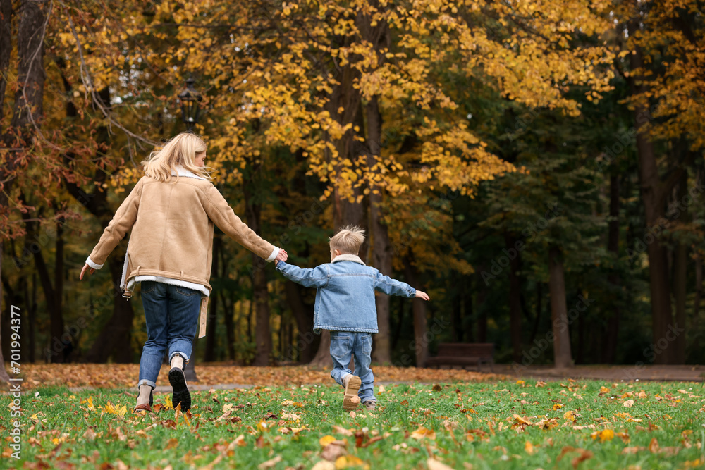 Fototapeta premium Mother running with her son in autumn park, back view. Space for text