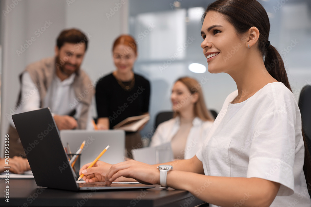 Team of employees working together in office. Happy businesswoman with laptop at table