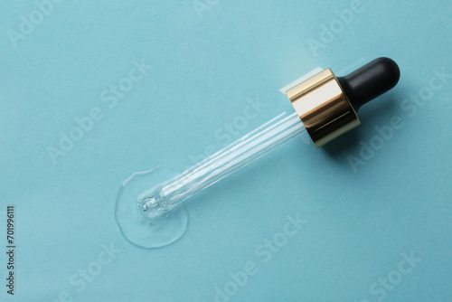 Clear cosmetic serum and pipette on light blue background, top view