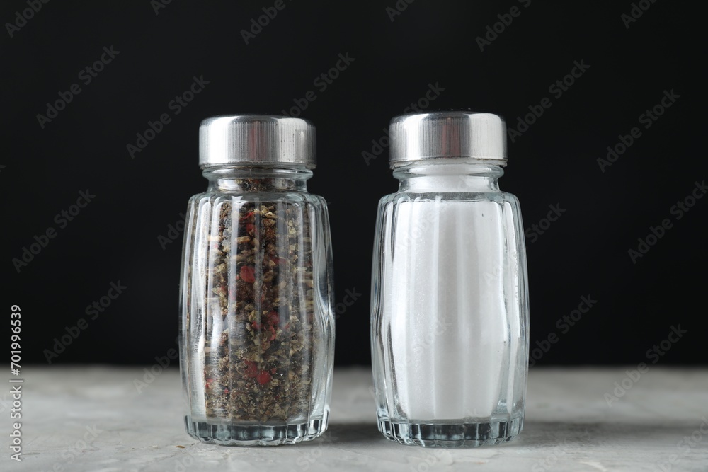 Salt and pepper shakers on light table against black background, closeup Salt and pepper shakers on light table against black background, closeup