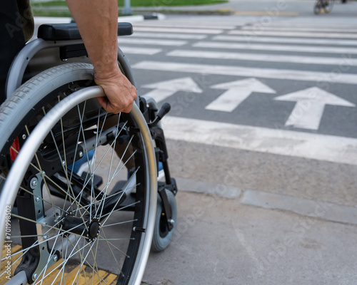 Rear view of an elderly woman in a wheelchair going to a pedestrian crossing. Close-up on wheels. 