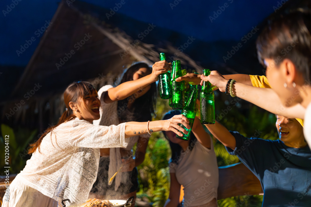 Fototapeta premium Group of Diversity Asian man and woman friends enjoy and fun celebration meeting dinner party eating barbecue grill and drinking beer together on lake house balcony on summer holiday vacation at night