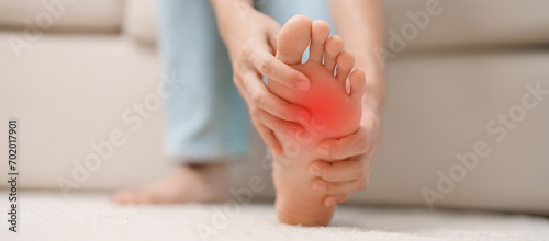 woman having barefoot pain during sitting on couch at home. Foot ache due to Plantar fasciitis and waking longtime. Health and medical concept photo