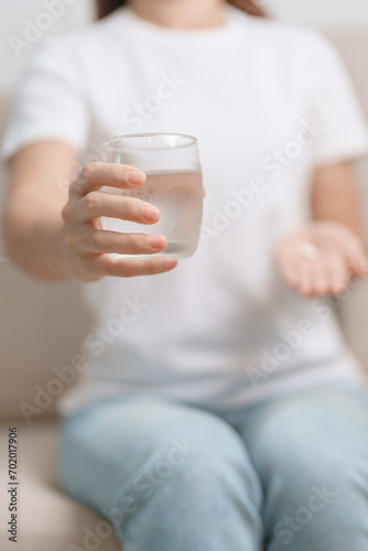 woman hand holding medicine painkiller pill and water glass on the sofa at home, taking for headaches, stomach ache, Diarrhea Pain from food poisoning, Endometriosis, Hysterectomy and Menstrual