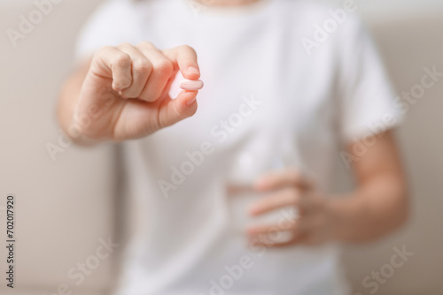 woman hand holding medicine painkiller pill and water glass on the sofa at home, taking for headaches,  stomach ache, Diarrhea Pain from food poisoning, Endometriosis, Hysterectomy and Menstrual photo