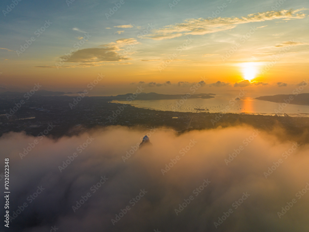 .aerial view bright yellow sun in sunrise at Phuket big Budha..Golden light illuminates the Buddha's head as it appears above the mist..A fluffy mist covers the Phuket Big Buddha.
