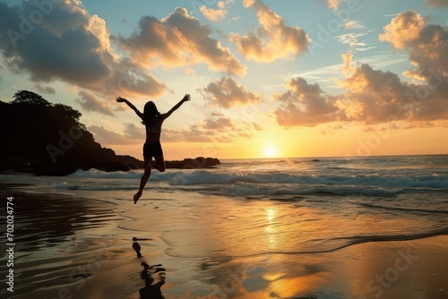 An inspired woman on the beach greets the day with a leap of joy, the sunrise painting a promising future for her continued success and happiness. photo