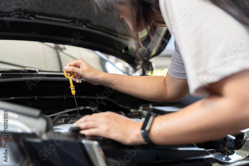 A woman pulls out the dipstick to check the oil level of her car, close-up photo of woman's hand check engine oil. © jittawit.21