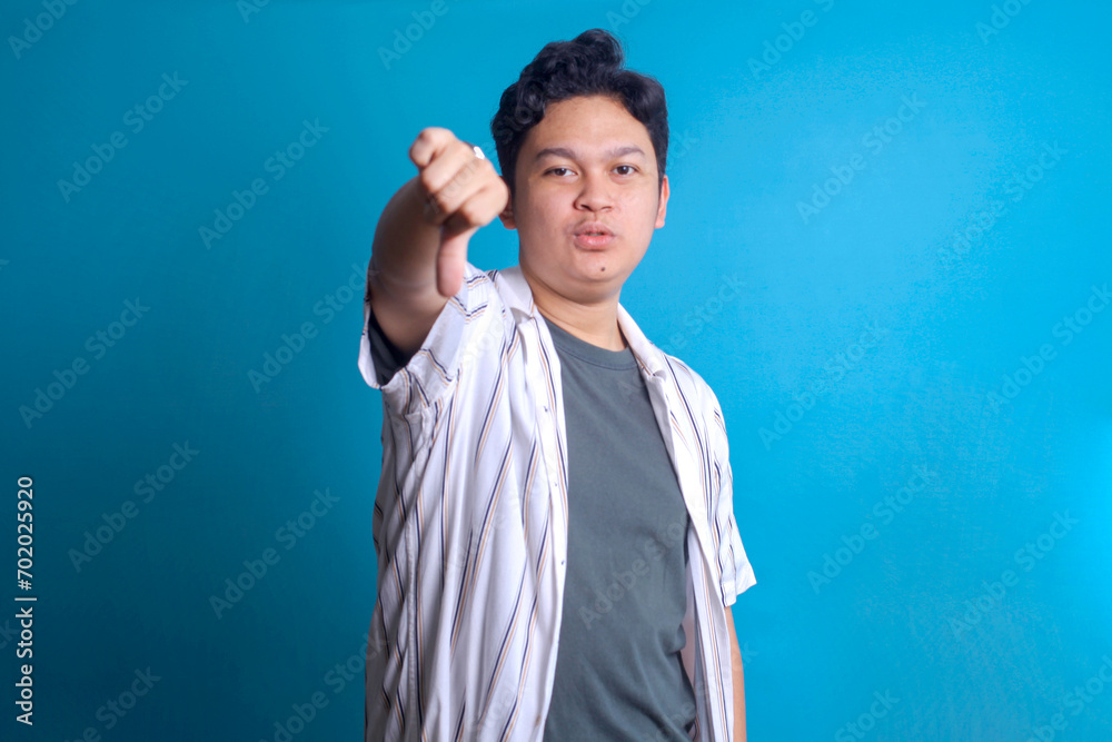 Disappointed Asian man showing negative sign with thumb down gesture Disappointed Asian man showing negative sign with thumb down gesture