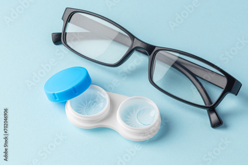 Contact lenses in case with solution liquid with eyeglasses on light blue background