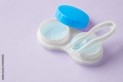 Contact lens on tweezer with solution liquid in case on pastel purple background
