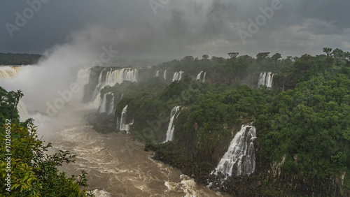 Breathtaking tropical waterfall landscape. Many streams of water collapse into the bed of a stormy river. Spray and fog rise into the sky like a cloud. Lush green vegetation all around. Iguazu Falls