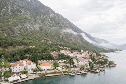 Ancient houses with red roofs at the foot of the mountains on the shores of the Bay of Kotor. Dobrota, Montenegro. Drone