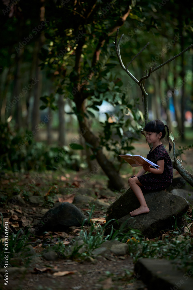 Little Child reading a book in a green coastal forest
