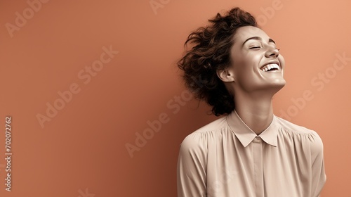 A joyful young woman in grayscale, standing against a minimalist coral-colored backdrop, her smile capturing a moment of pure happiness