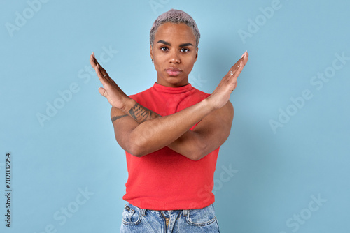 Young brave African American woman makes prohibiting gesture by crossing arms and looks at screen with serious grimace refusing to cooperate or declaring boycott stands on turquoise background.