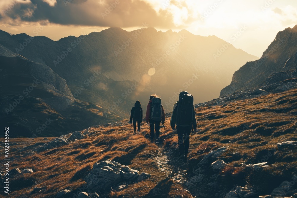 Group of hikers trekking in mountainous terrain at sunset, with warm sunlight casting long shadows.