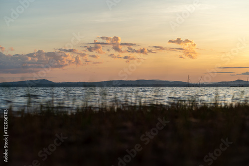 Morning waterfront view of Sirindhorn Dam Beach. We can see beach grass, river waves, and mountains.