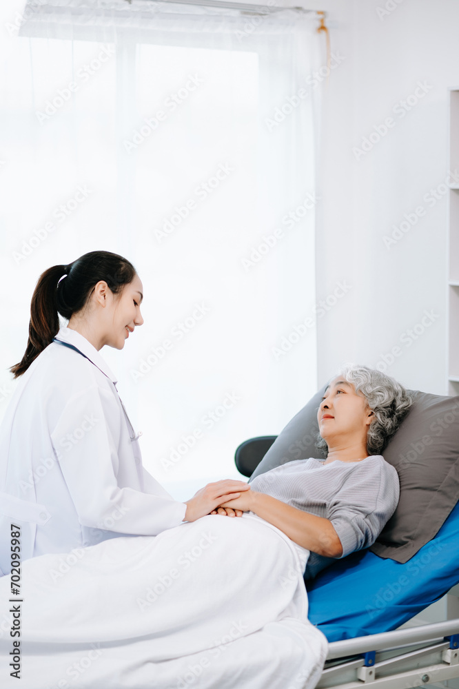Doctor in white suit take notes while discussing and Asian elderly, woman patient who lying on bed with receiving saline solution