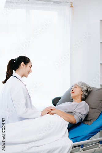 Doctor in white suit take notes while discussing and Asian elderly, woman patient who lying on bed with receiving saline solution